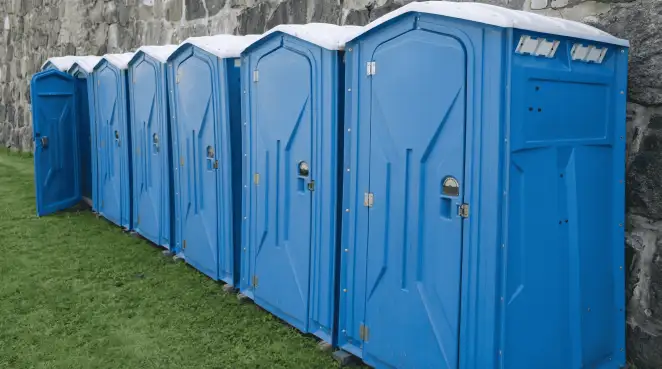 Row of blue portable toilets lined up on grass against a stone wall for event sanitation in Oakland, CA
