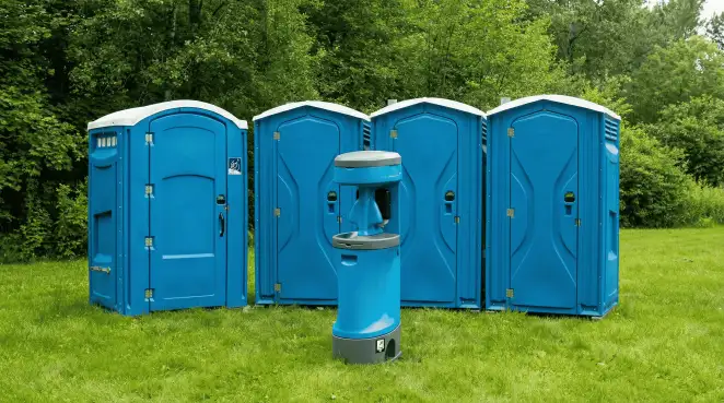 Four blue portable toilets and a matching hand washing station on grass near trees, a common sight at local outdoor events in Oakland, CA