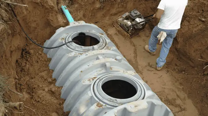 Septic tank installation showing a technician compacting soil around a new poly septic tank in an excavation pit in Oakland, CA